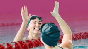 Two smiling female swimmers in a pool give a high-five at the end of a swim meet.