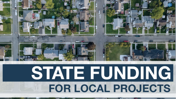 STATE FUNDING FOR LOCAL PROJECTS, in white and blue text on a blue and white background, in front of a bird’s-eye view photo of a neighborhood.